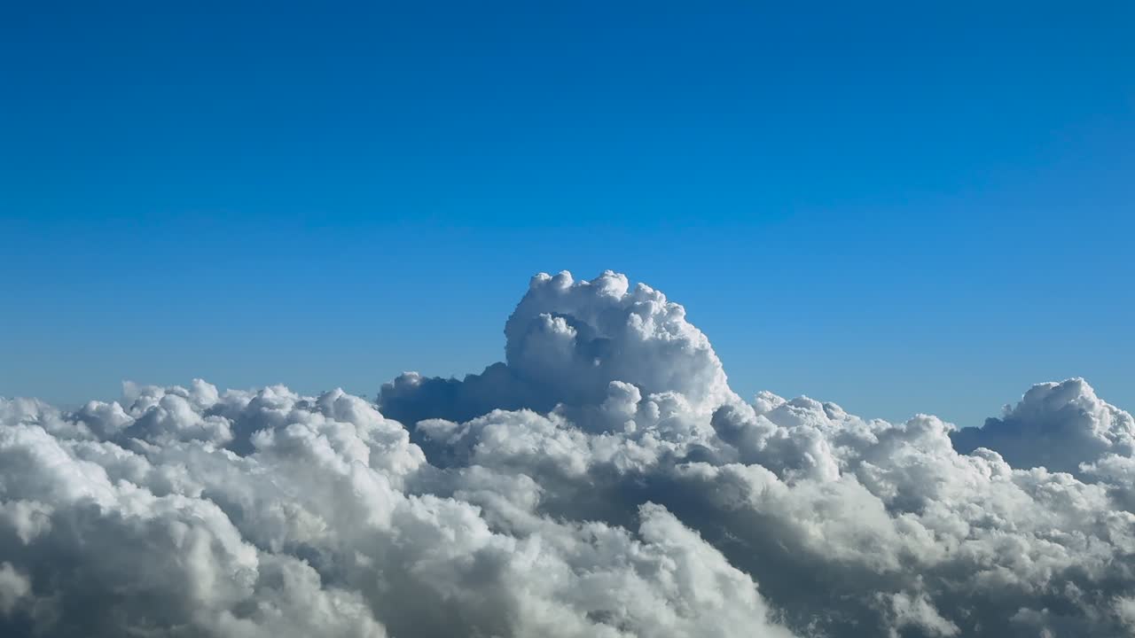 An immersive pilot’s eye perspecvtive taken from the cockpit of a jet airplane flying above a cottony storm clouds under a deep blue sky