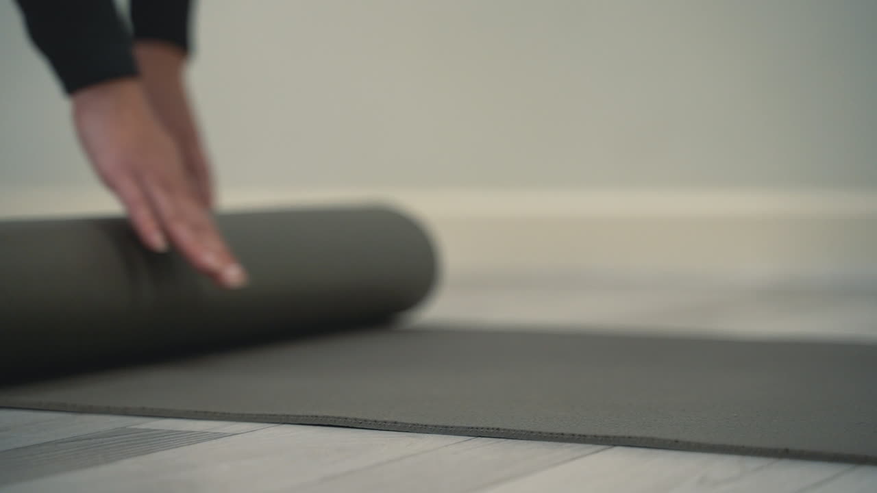 mujer joven desenrolla la alfombra de yoga en el suelo y se prepara para meditar y hacer ejercicios. primer plano.