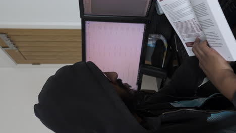 uk asian male wearing hoodie and glasses reading book at desk at home