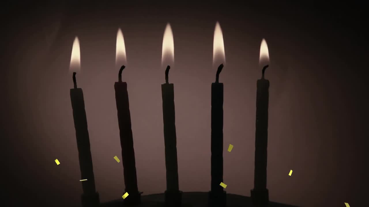 Coriandoli dorati che cadono sopra la silhouette di diverse candele accese su sfondo grigio.