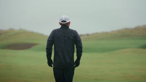 golfer surveying approach shot from fairway, places hands on hips in rain in slow motion