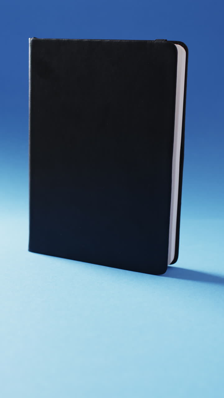 Vertical video of closed black book vertical with copy space on blue background in slow motion
