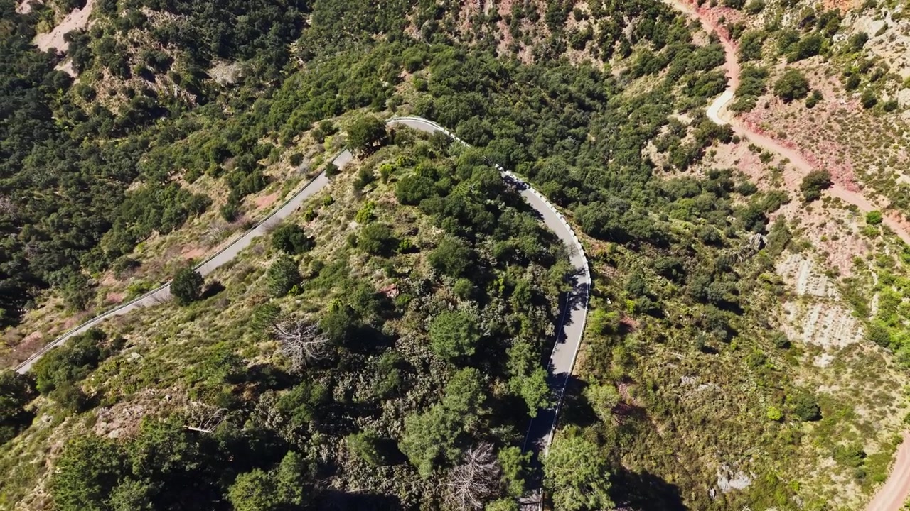 Carretera sinuosa a través de colinas verdes en una zona montañosa durante el día.