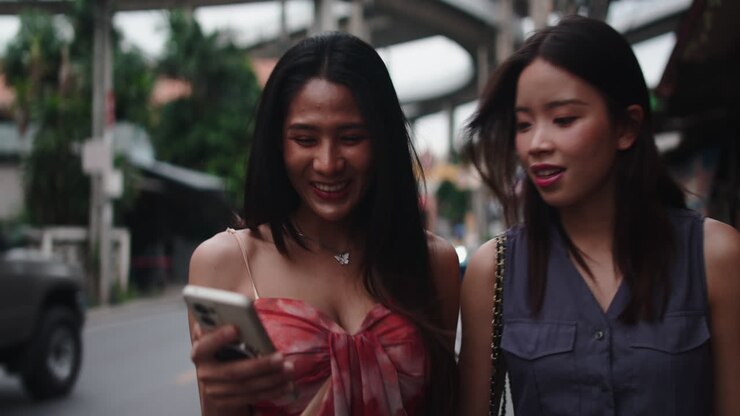 To smilende kvinder, der kigger på en mobiltelefon på gaden