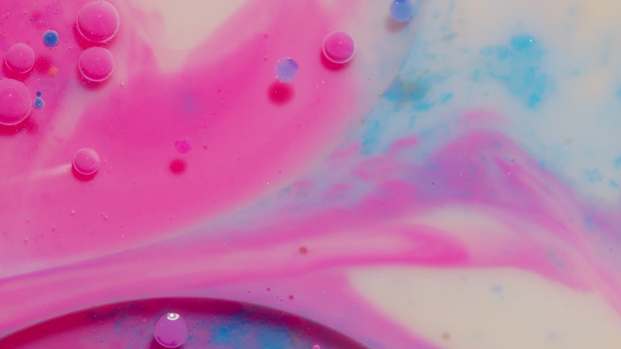 Movimiento de burbujas de gotas de tinta de aceite rosa visto desde arriba, sobre un fondo de superficie de pintura artística multicolor.