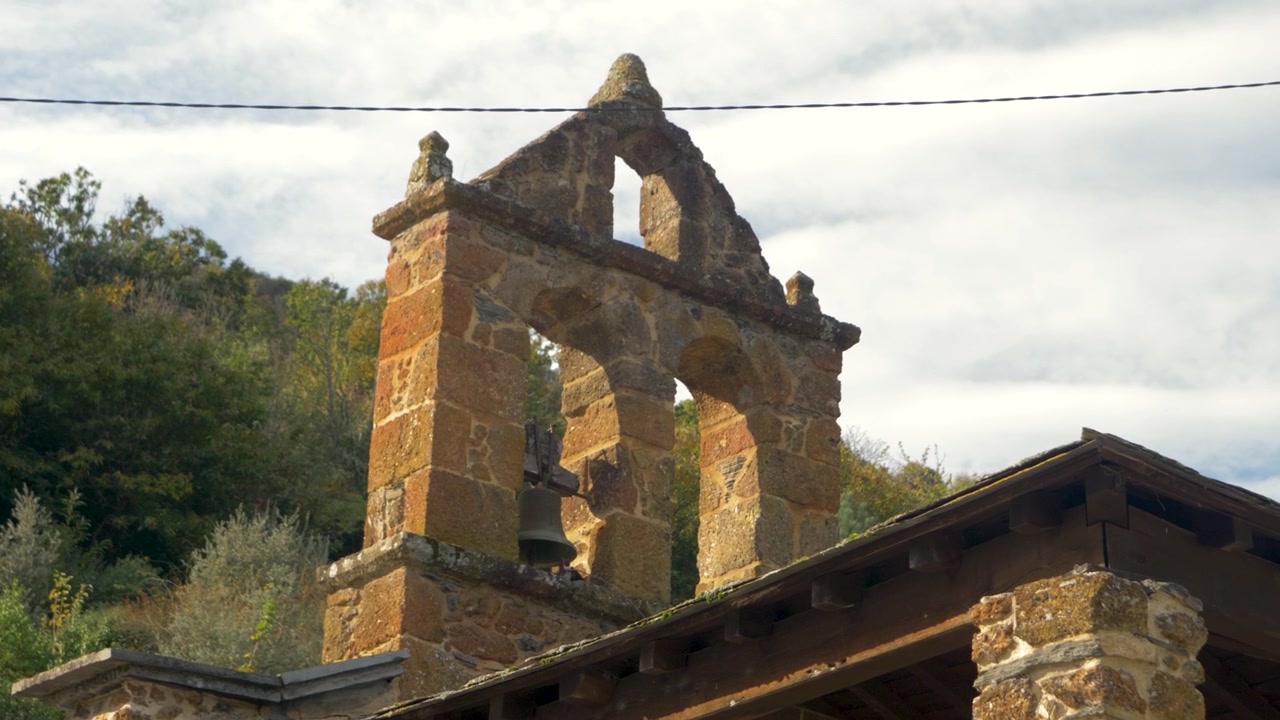 Empena de sino em pedra e aberturas duplas para sinos erguem-se sobre a Igreja de Penouta em Vilamartín de Valdeorras