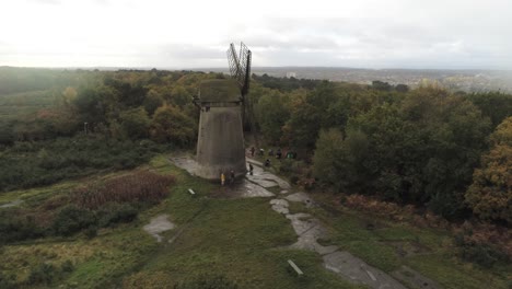 Traditional-wooden-stone-flour-mill-windmill-preserved-in-Autumn-woodland-aerial-view-countryside-dolly-right-in-rain