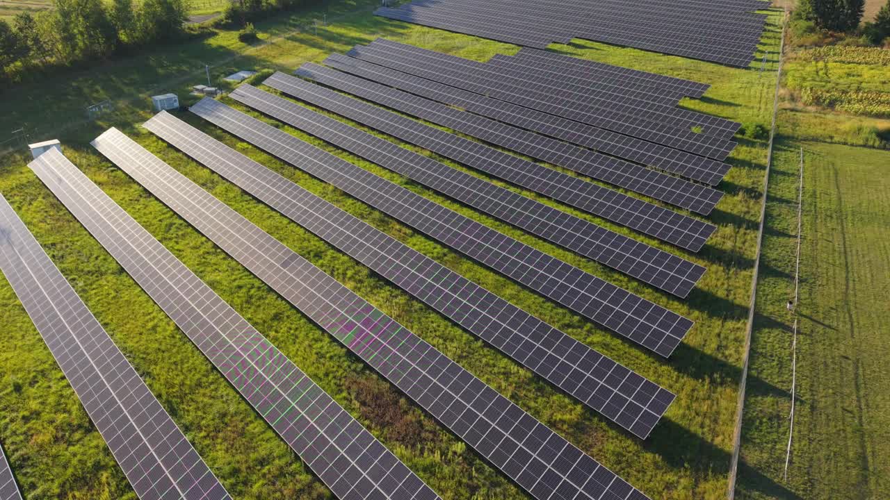 A drone video of a solar energy farm with rows of photovoltaic panels installed on green grass. The video illustrates renewable energy production and sustainable power generation technology