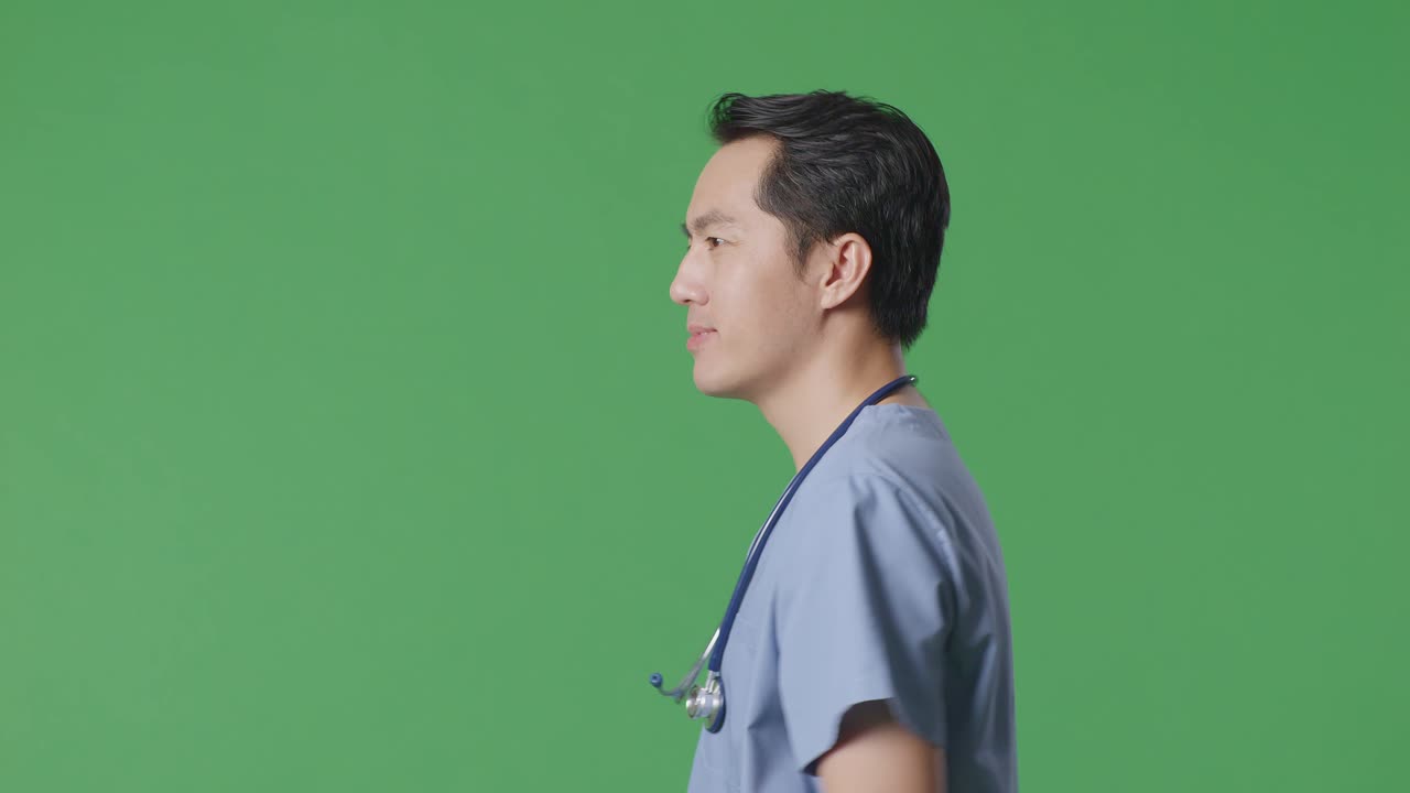 Close Up Of Side View Asian Male Doctor With Stethoscope Waving Hand And Smiling While Walking On Green Screen Background In The Hospital