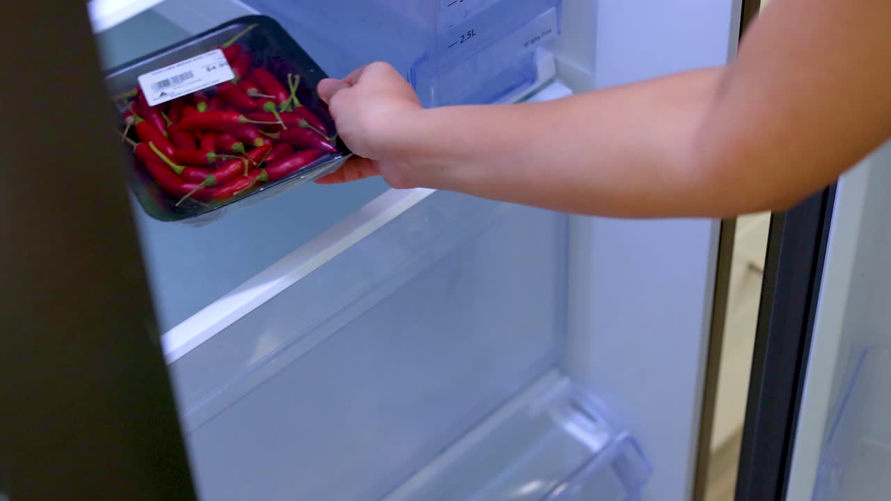 A person arranges vegetables in a refrigerator, focusing on organization and freshness. Bright lighting enhances the clean, modern kitchen setting