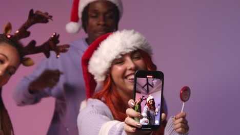 Foto-De-Estudio-De-Amigos-De-La-Generación-Z-Bailando-Y-Posando-Para-Un-Selfie-En-Una-Fiesta-De-Navidad-Con-Gorro-De-Papá-Noel-Y-Astas-De-Reno.