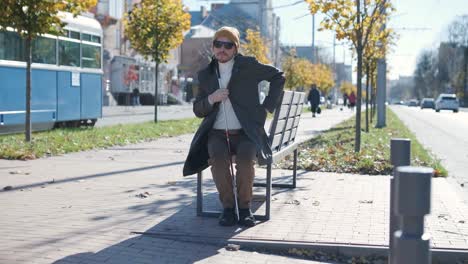 young blind man with smartphone sitting on bench in park in city, calling