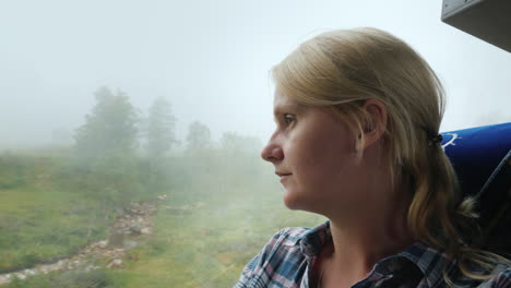 a woman looks out the window of a bus to a forest covered with thick fog traveling in norway