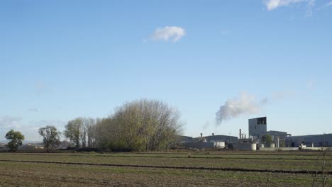 static shot of a rural farming industry emitting polluting fumes in an organic farming area