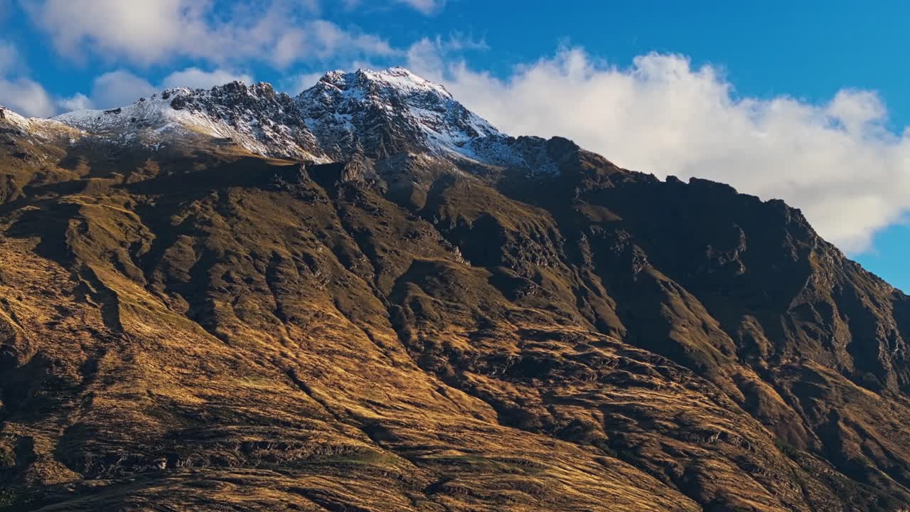 las nubes se reúnen detrás del pico nevado en la roca de piedra arenisca oscura bajo el cielo azul
