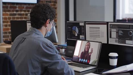 Caucasian-man-on-laptop-video-chat-wearing-face-mask-in-office