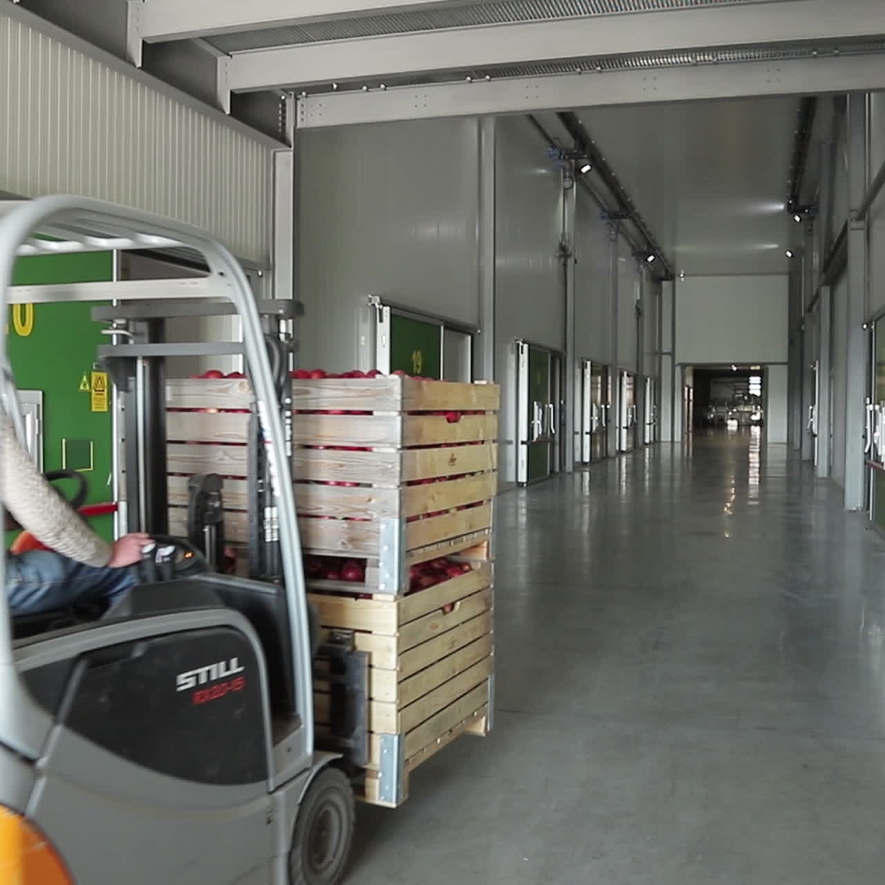 A man on the loader carries two wooden boxes with red apples along the corridor for storage in the warehouse. Retail.