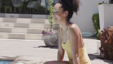 portrait of happy african american woman sitting by swimming pool, slow motion