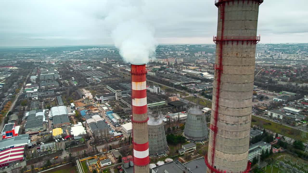 Aerial drone view of thermal power plant in Chisinau at cloudy weather, Moldova. View of pipes with felling steam, buildings and yellowed trees around
