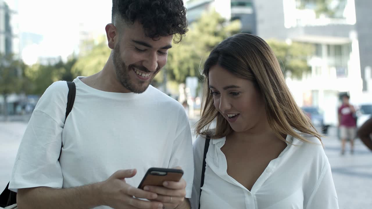 una joven pareja sonriente mirando un teléfono inteligente