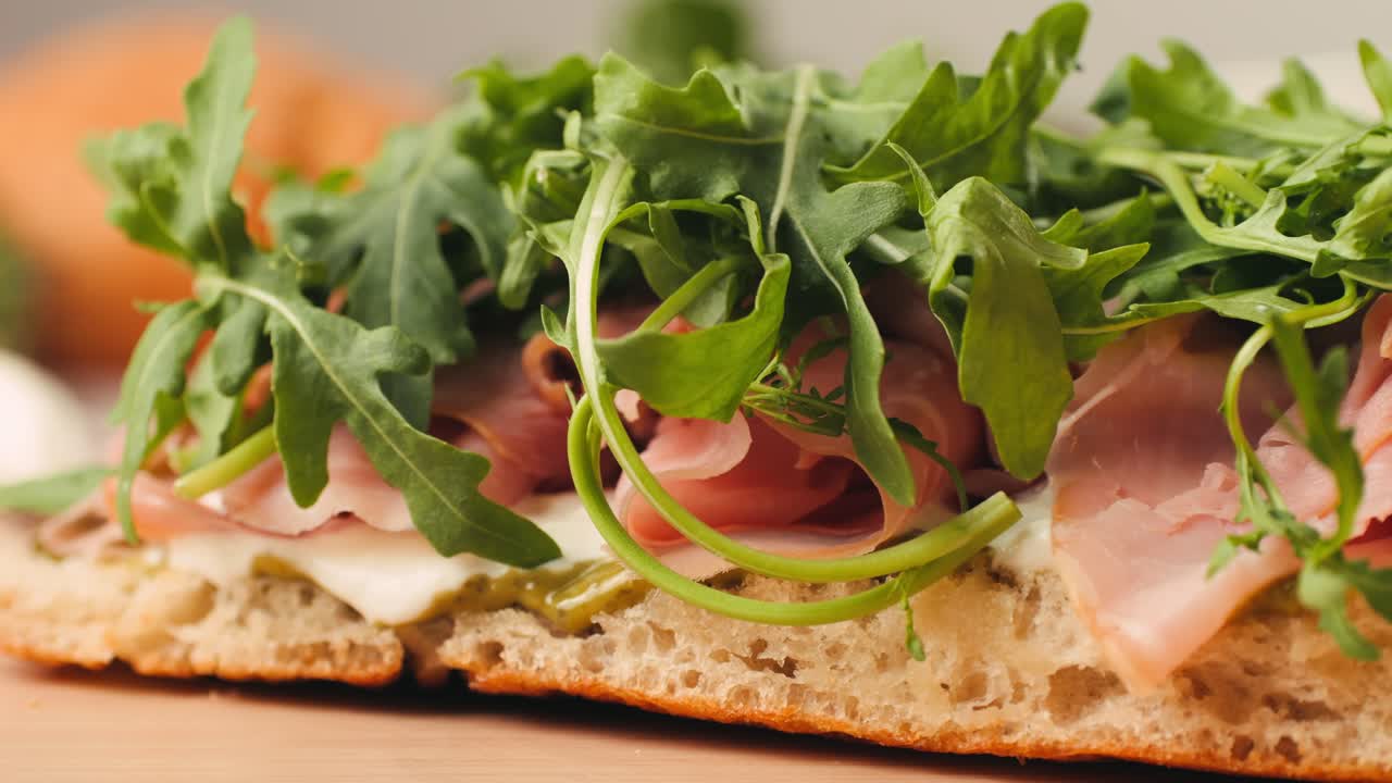 Mortadella ham sandwich, Traditional italian focaccia filled with thin pesto slices of mortadella, served by chef man in cafe restaurant. Macro of traditional italian spanish tapas antipasti.