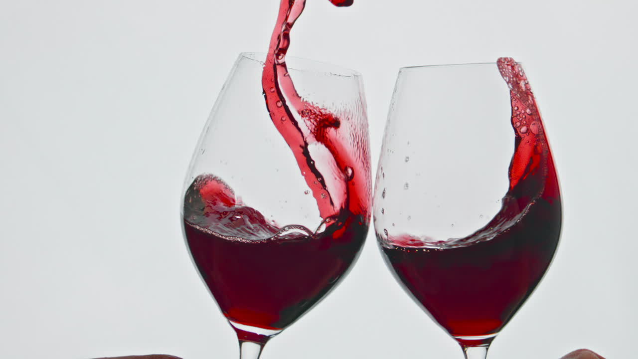 Primo piano di bicchieri di bevanda rossa che tintinnano e vengono sollevati. Vino rosato che schizza oltre il bordo.