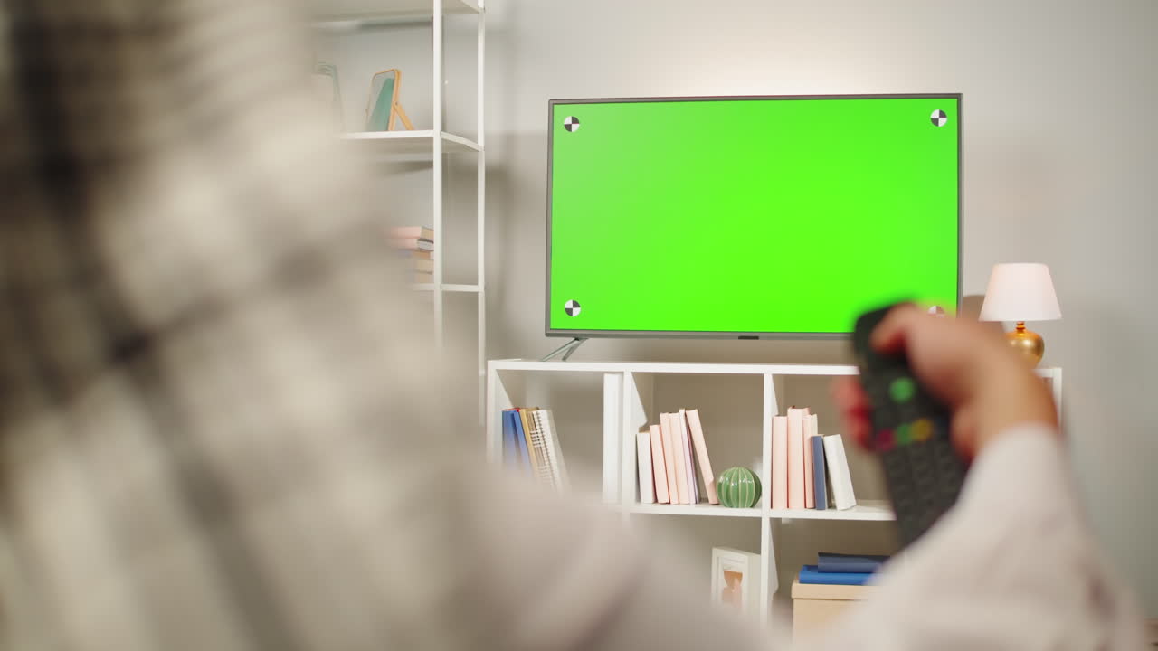 Middle eastern man watching tv with chroma key close-up. Person watches television with green screen in living room. Wearing traditional Islamic clothes
