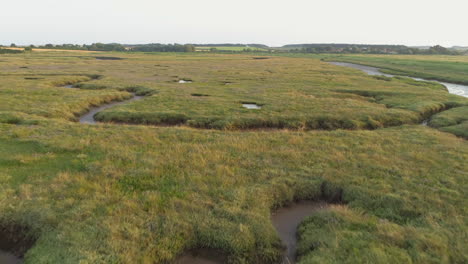 low aerial drone shot flying over fairly dry green salt marsh at sunset in north norfolk uk