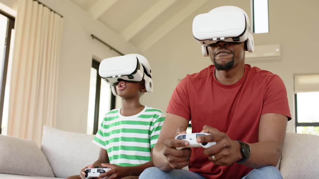 Padre e figlio afroamericani che prendono visori VR e controller per giocare sul divano del soggiorno