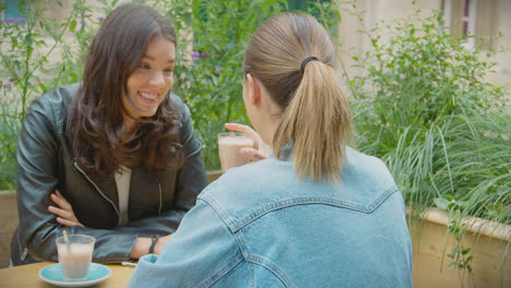 happy same sex female couple meeting and sitting outdoors at coffee shop together