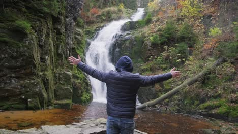 a figure stands before a waterfall embracing natures beauty. a figure stands before a waterfall, embracing natures beauty with outstretched arms. clad in a hooded jacket, he reflects on outdoor experiences