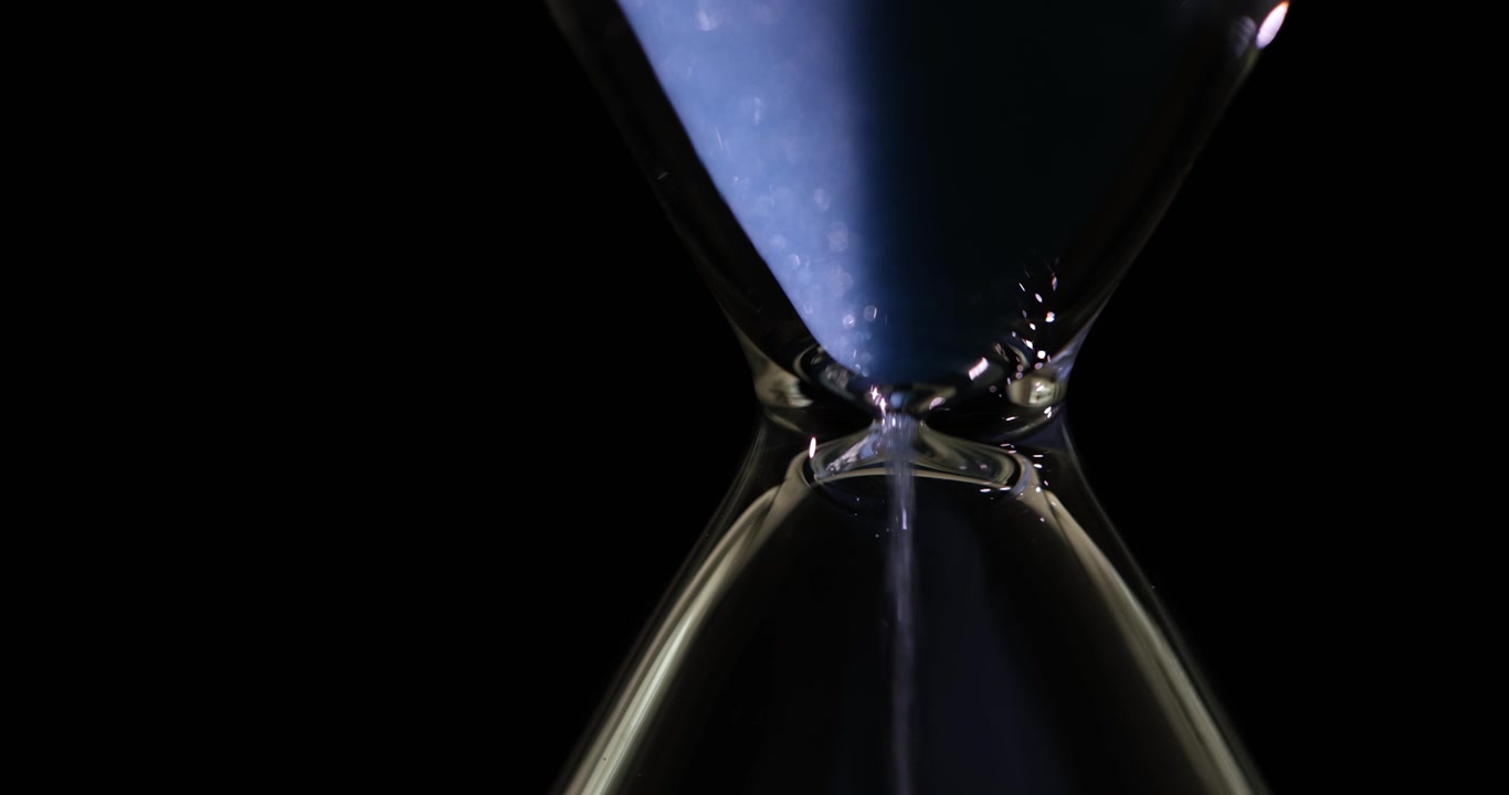 Blue sand steadily falls from top chamber of hourglass