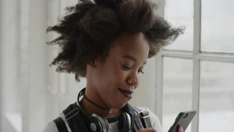 Retrato-De-Cerca-De-Una-Mujer-Afroamericana-Usando-Mensajes-De-Texto-En-Un-Teléfono-Inteligente-Navegando-Disfrutando-De-Mensajes-En-Las-Redes-Sociales-En-Línea-En-El-Fondo-De-La-Ventana-Del-Apartamento