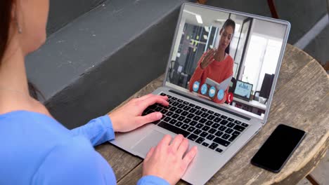 mujer de negocios caucásica sentada en un escritorio usando una computadora portátil haciendo una videollamada con una colega