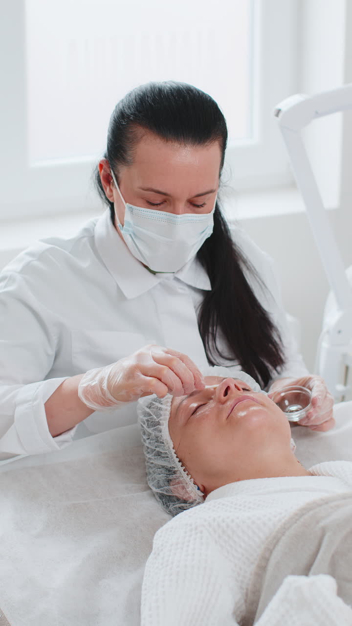 Cosmetologist applying special moisturizing acid serum peeling face nose of young woman in clinic