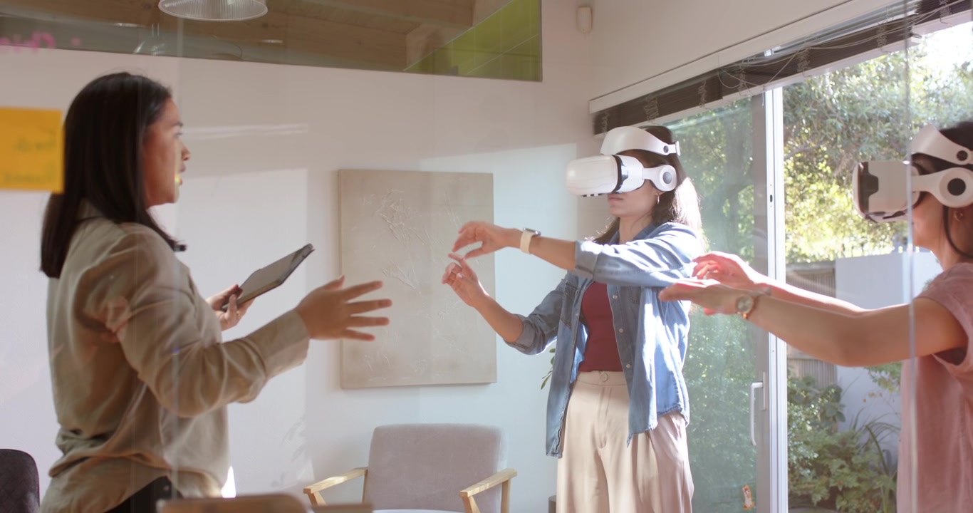 Guida femminile che conduce una sala riunioni con un tablet al centro, una donna che prende un visore VR bianco seguendo le indicazioni.