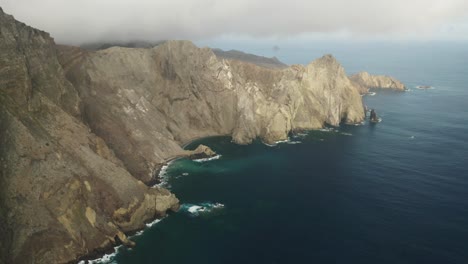 Scenic-steep-cliffs-of-Porto-Santo,-rugged-shore-at-Atlantic-Ocean,-aerial