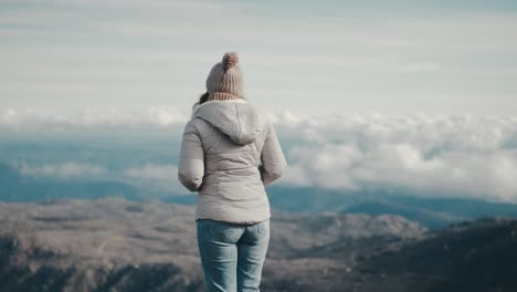 a young caucasian woman turns her back to the camera and gazes at the mountain landscape