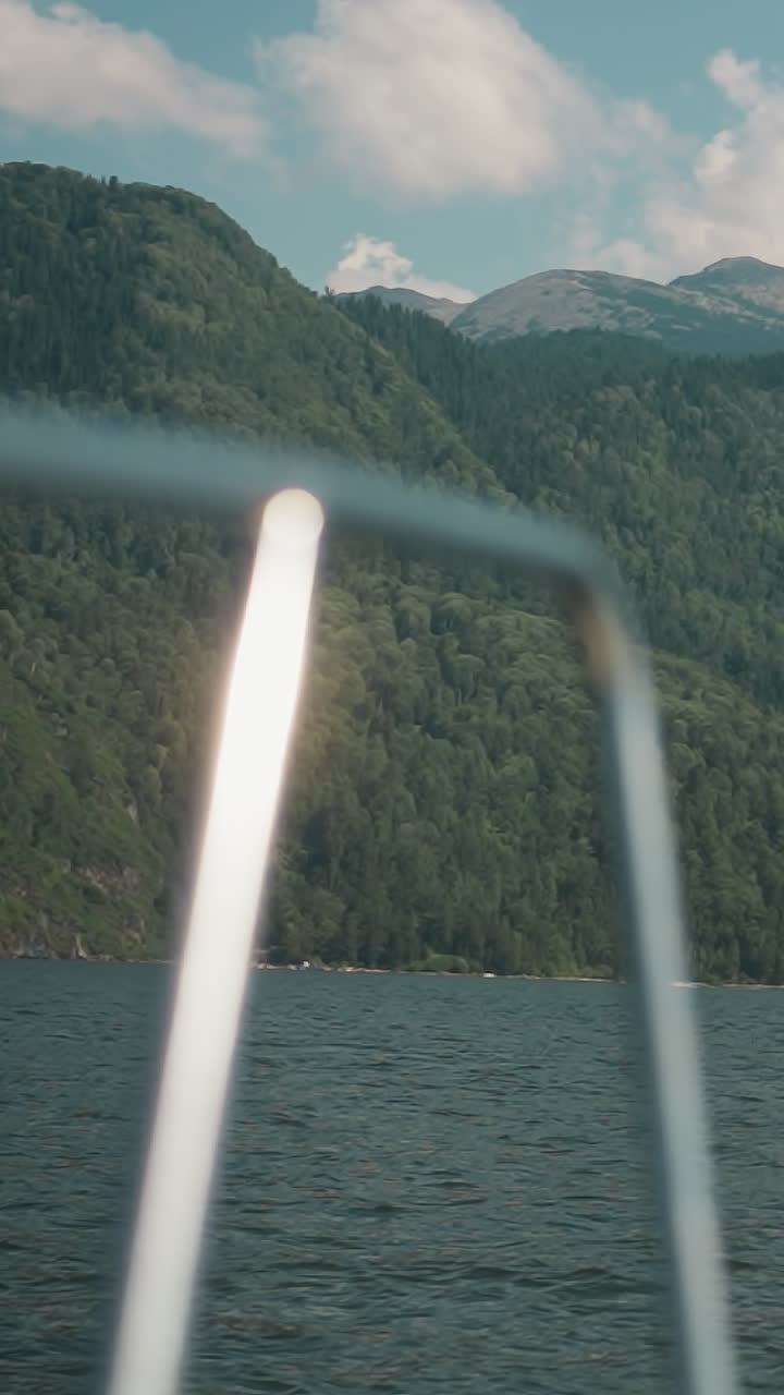 호수 연안에 있는 큰 푸른 산들, 구름이 은 하늘 아래, 요트 뒷면에서 볼 수 있는 풍경, 모터 보트에서 그림 같은 야생 자연으로 여행, 해안과 바다 만에 있는 오래된 산꼭대기.