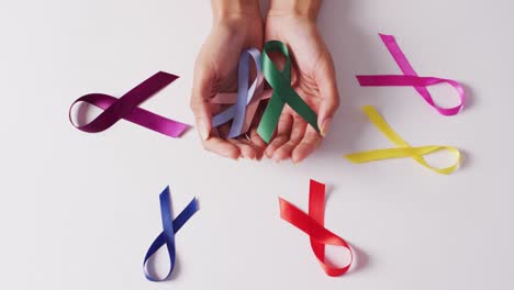 Video-of-hands-of-caucasian-woman-holding-colorful-ribbons-on-white-background