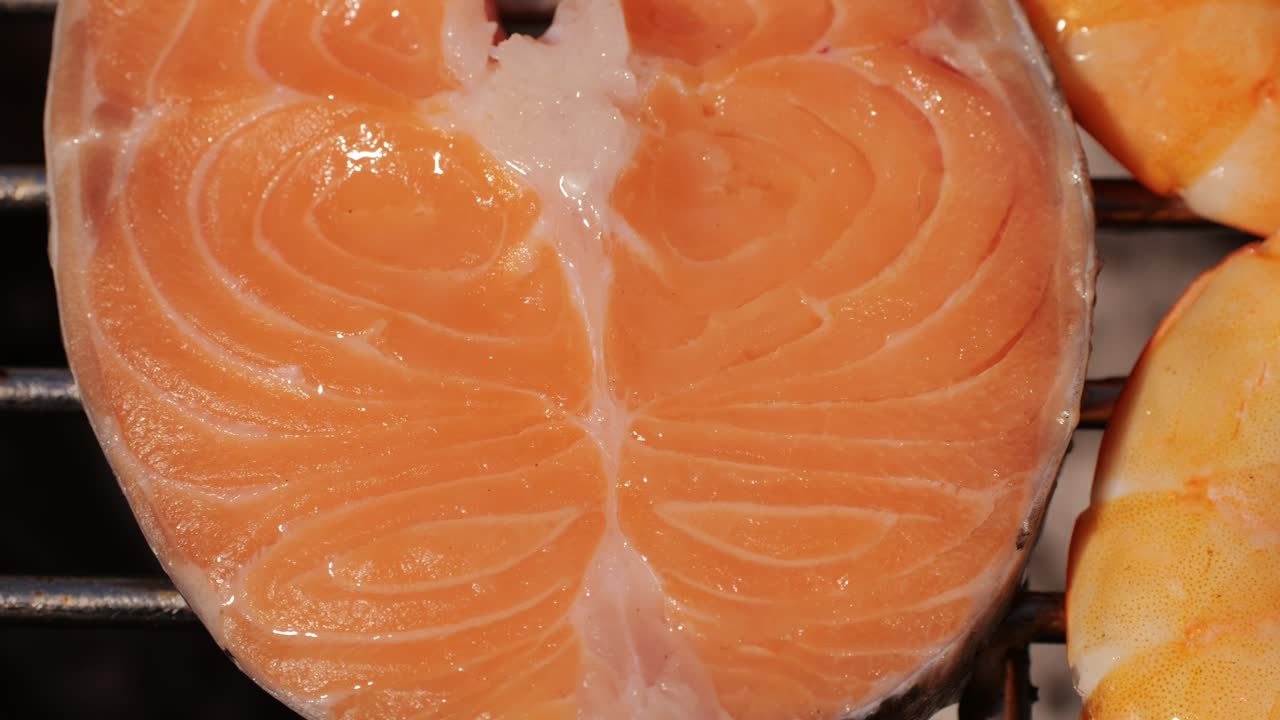 Chef cooking red salmon fish steaks with oil and spices on grill close-up. Prawns on fire throwing them on pan. Making Dorado fishes on frying grill. Restaurant Food concept. Sea food barbecue.