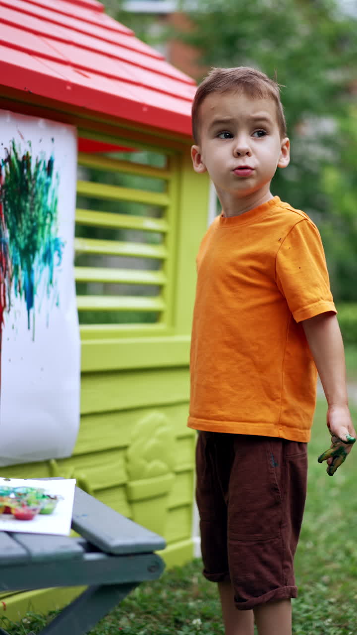 Beautiful kid painting a picture with his fingers. Kid uses colorful paints applying them on the white piece of paper. Vertical video.