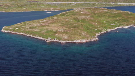 Aerial-crane-shot-pivots-down-over-the-shoreline-of-a-small-green-island-in-a-Fjord-in-Haukelifjell-Norway