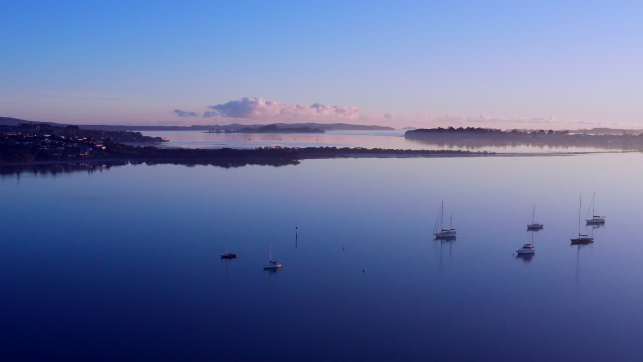 뉴질랜드 오클랜드의 잔잔한 해변에 햇빛이 반사되면서 물 위에 떠 있는 요트