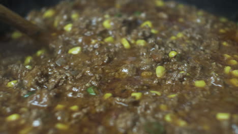 wooden spoon stirring mince meat with sweetcorn and fresh chillies