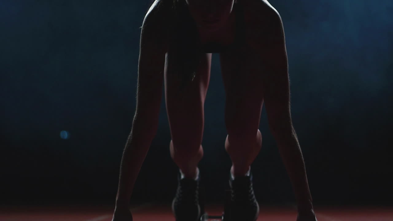 Female athlete on a dark background is preparing to run the cross-country sprint from the pads on the treadmill on a dark background