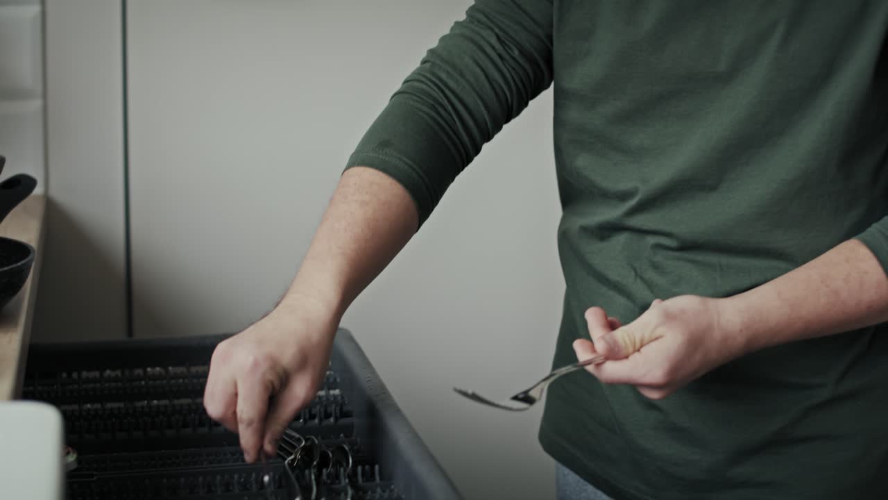 взрослый мужчина с синдромом дауна загружает посудомоечную машину дома в одиночку.