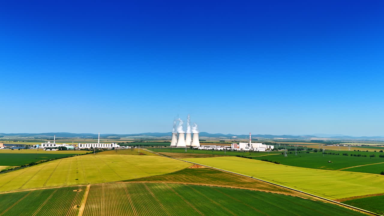 Power plant in green fields. A nuclear power plant is visible, surrounded by lush fields under a clear blue sky, showcasing energy production