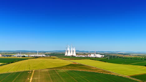 power plant in green fields. a nuclear power plant is visible, surrounded by lush fields under a clear blue sky, showcasing energy production