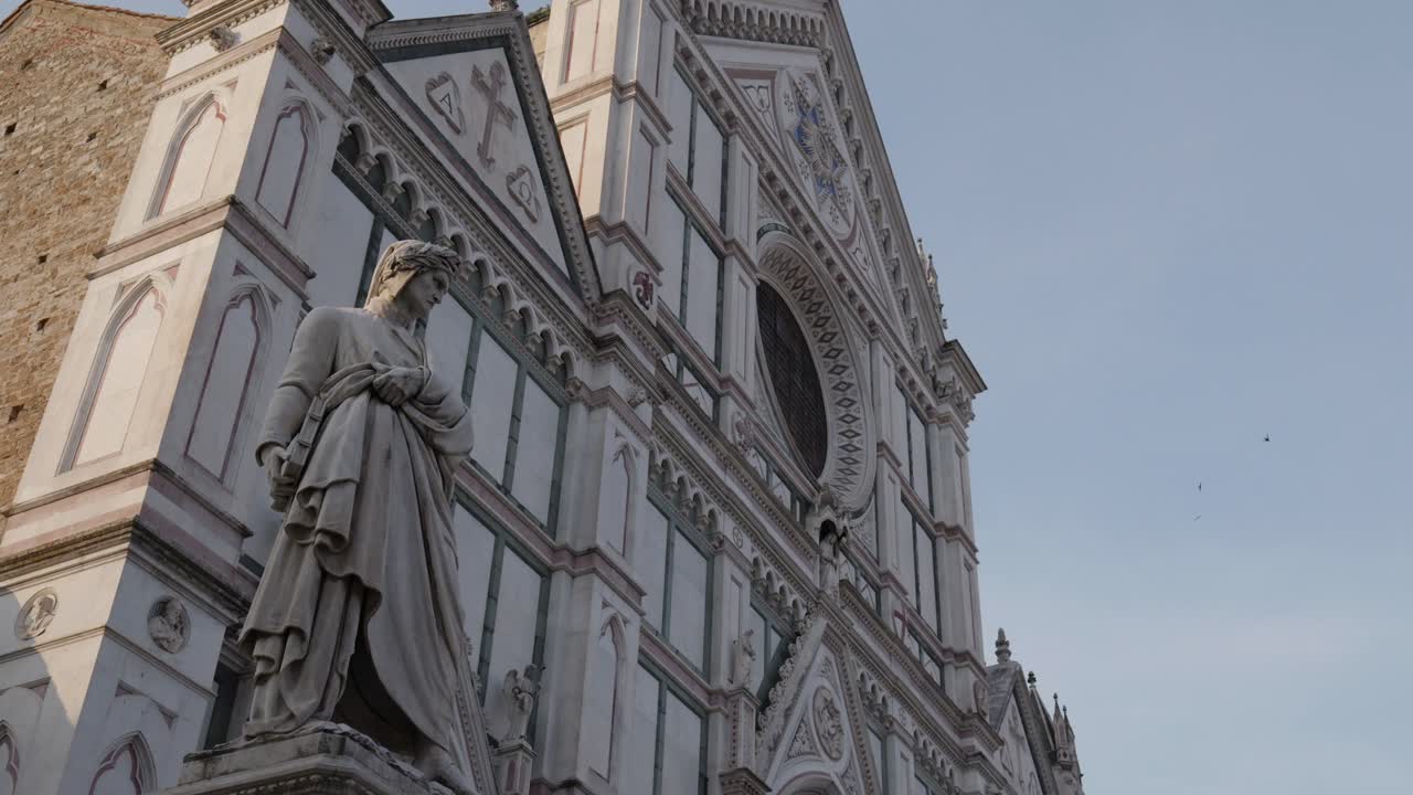 덴테 알리기에리의 동상 머리에 로 ⁇  꽃받침과 그의  ⁇ 에 독수리가 피렌체에 있으며 배경에는 산타 크로세 대성당이 있습니다.